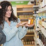 woman and man reading back of raw honey jar in grocery store